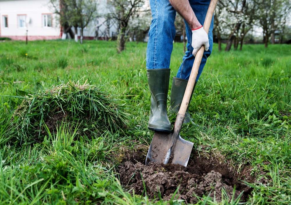 A man wearing boots digging in the soil with a shovel