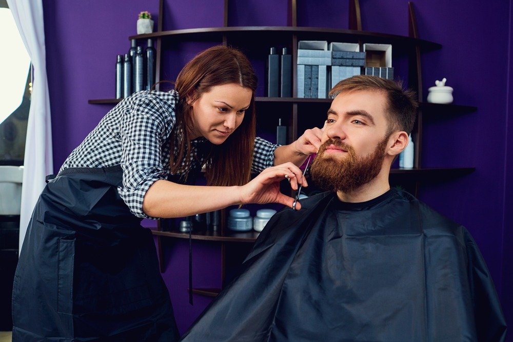 a lady cutting man's beard using scissor in a salon